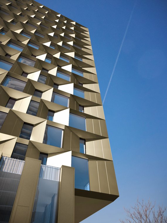 Close-up of the striking golden facade of The Molecules Berlin with geometric window elements against a blue sky, architectural 3D Visualization by gmsvision.