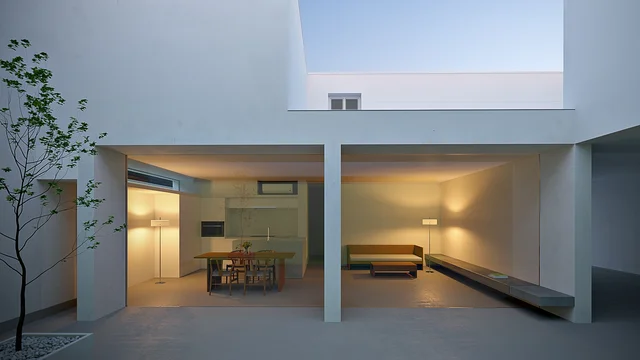 3D Visualization of a modern courtyard in the White Cave House in Japan, minimalist white architecture with open living and dining area, warmly illuminated at dusk.