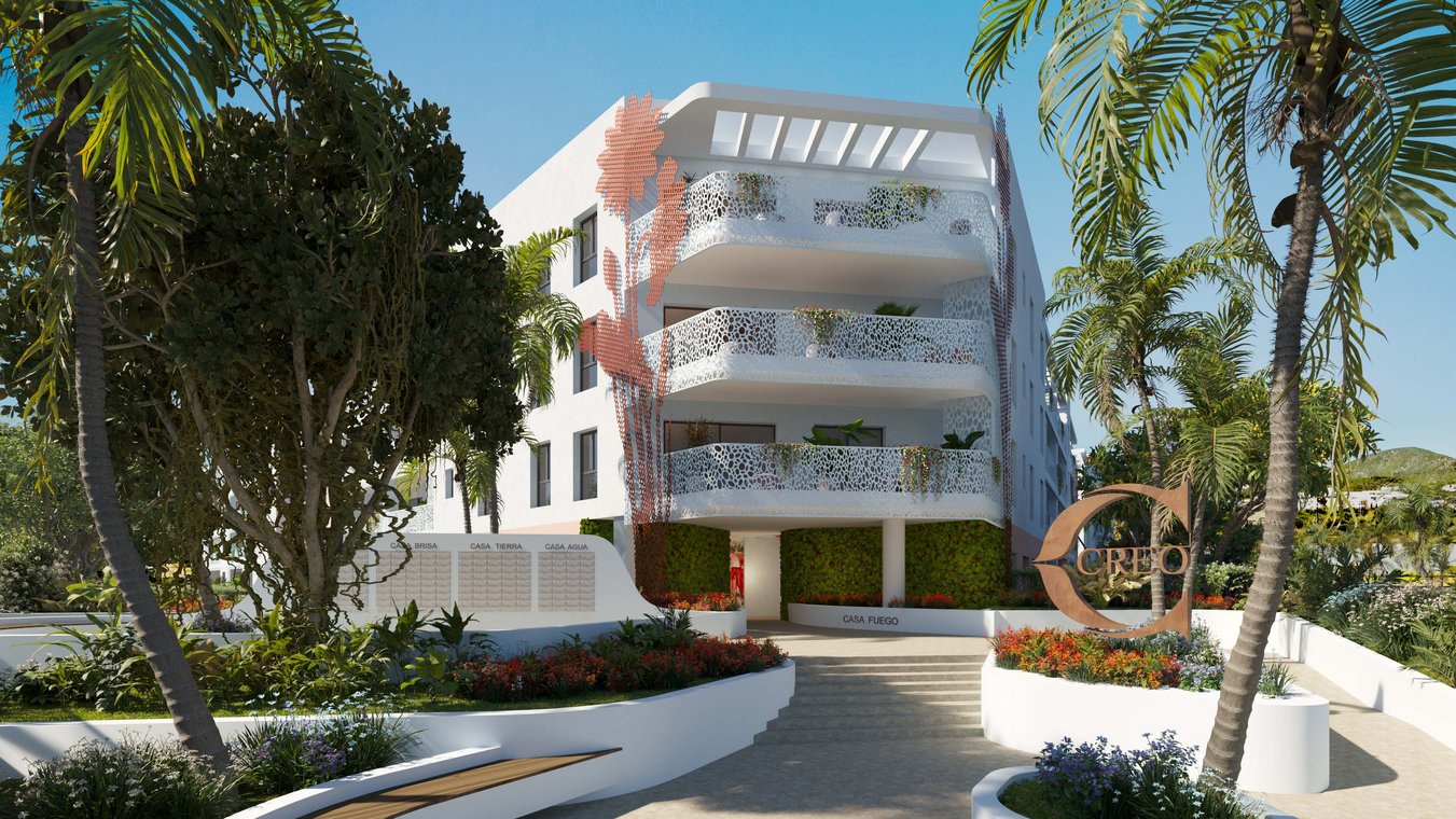 3D visualization of the entrance area of CREO Ibiza with modern white buildings, decorative balcony railings, lush tropical plants, vibrant flower beds, and the stylish CREO logo in the foreground