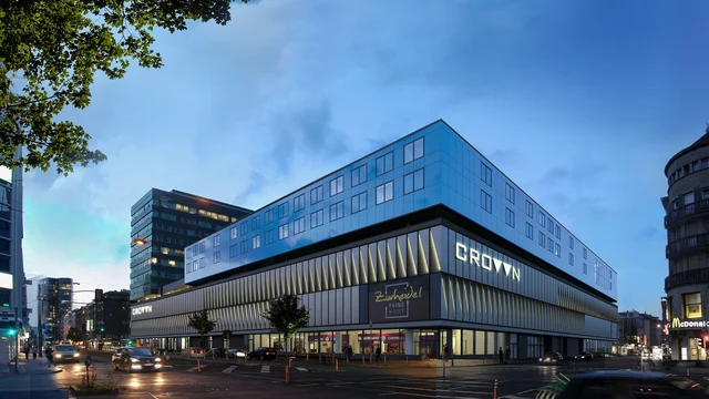 Architectural Visualization of the Crown Düsseldorf building at dusk, featuring illuminated glass façade, glowing signage, and vibrant city atmosphere.