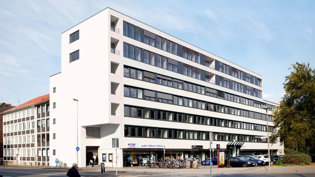 Architectural Visualization of the modern residential and commercial building at Blissestraße 5 in Berlin, featuring a clean white façade, large window fronts, and an urban street setting.
